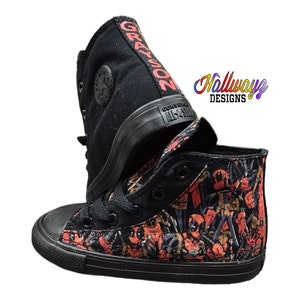 May include: Black high-top Converse sneakers with a custom design featuring a repeated pattern of Deadpool characters. The shoes have a black sole and black laces. The words "GRAYSON" are written on the side of one shoe.