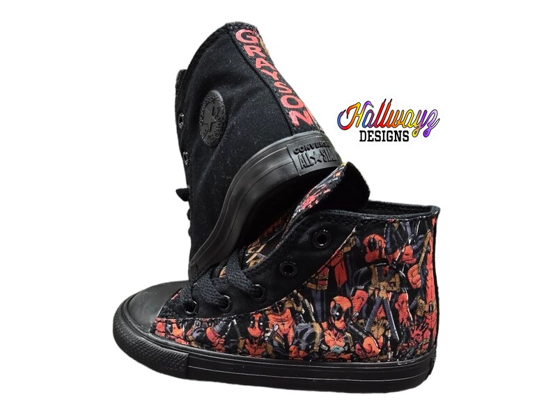 May include: Black high-top Converse sneakers with a custom design featuring a repeated pattern of Deadpool characters. The shoes have a black sole and black laces. The words "GRAYSON" are written on the side of one shoe.