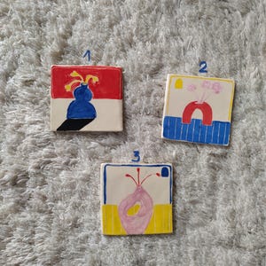 May include: Three ceramic tiles with colorful abstract floral designs. Each tile features a different vase shape and floral arrangement in shades of red, yellow, blue, and pink.