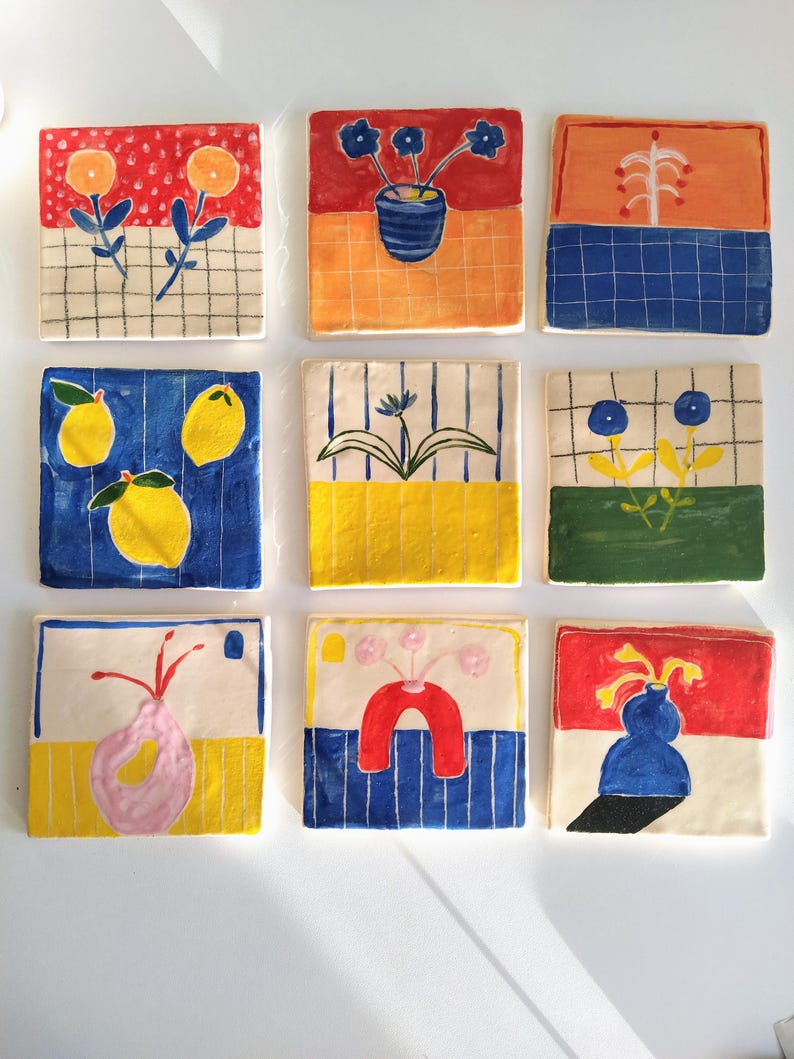 May include: Nine ceramic tiles with colorful abstract designs. Each tile features a different combination of colors and shapes, including red, blue, yellow, green, and white. The tiles are arranged in a grid pattern.