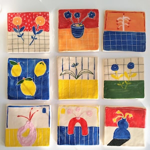 Puede incluir: Nueve azulejos de cerámica con diseños pintados a mano de colores. Cada azulejo presenta un patrón floral o geométrico diferente, incluyendo limones, flores y jarrones. Los azulejos son perfectos para agregar un toque de fantasía a cualquier espacio.
