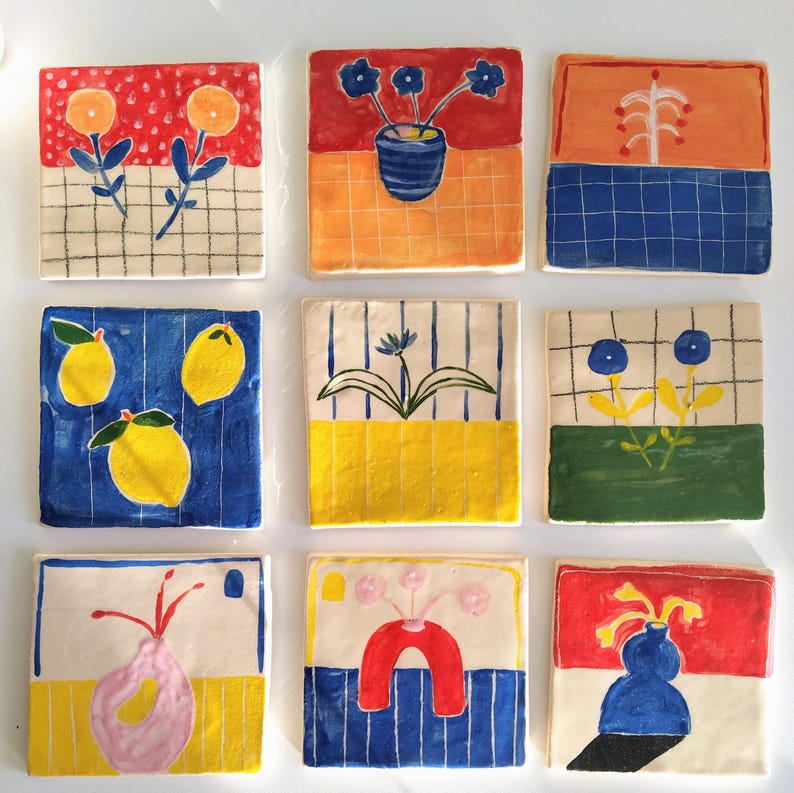 May include: Nine ceramic tiles with colorful hand-painted designs. Each tile features a different floral or geometric pattern, including lemons, flowers, and vases. The tiles are perfect for adding a touch of whimsy to any space.