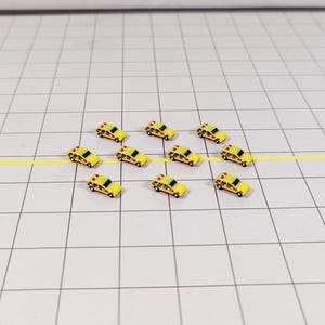 May include: Nine miniature yellow toy cars with black accents and red lights on top, lined up in two rows on a white grid surface.