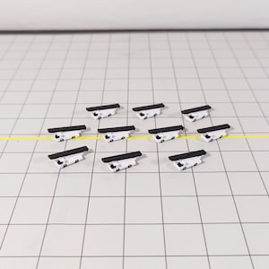 Könnte beinhalten: Eine Ansammlung von zehn kleinen, weiß-schwarzen Objekten, die auf einem Raster angeordnet sind. Jedes Objekt hat eine rechteckige schwarze Oberseite und eine weiße Basis mit kleinen Details. Die Objekte sind gleichmäßig verteilt.