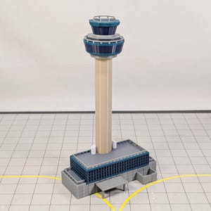May include: A detailed model of an airport control tower. The tower features a beige cylindrical body, a gray base, and a blue and gray control room at the top. The model is set on a grid-patterned surface.
