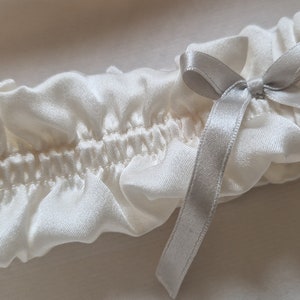 Soft white, pure silk wedding garter adorned with a graceful silver silk bow at its centre.

This image is a close-up view, showing the meticulous stitching and delicate silk ribbon attached to the centre of the gater.