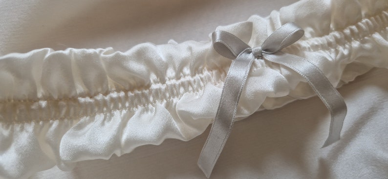 Soft white, pure silk wedding garter adorned with a graceful silver silk bow at its centre.

This image is a close-up view, showing the meticulous stitching and delicate silk ribbon attached to the centre of the gater.