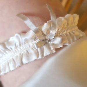 Soft white, pure silk wedding garter adorned with a graceful silver silk bow at its centre.

This image is a close-up of the wedding garter being worn.