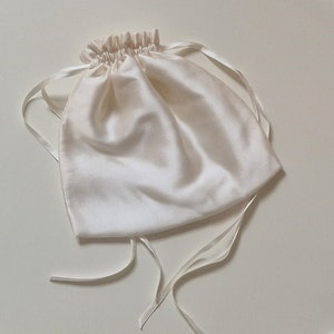 Image of drawstring silk bag which comes with the wedding garter. It is made from soft white silk, with long narrow silk ribbons and is shown closed and gathered.