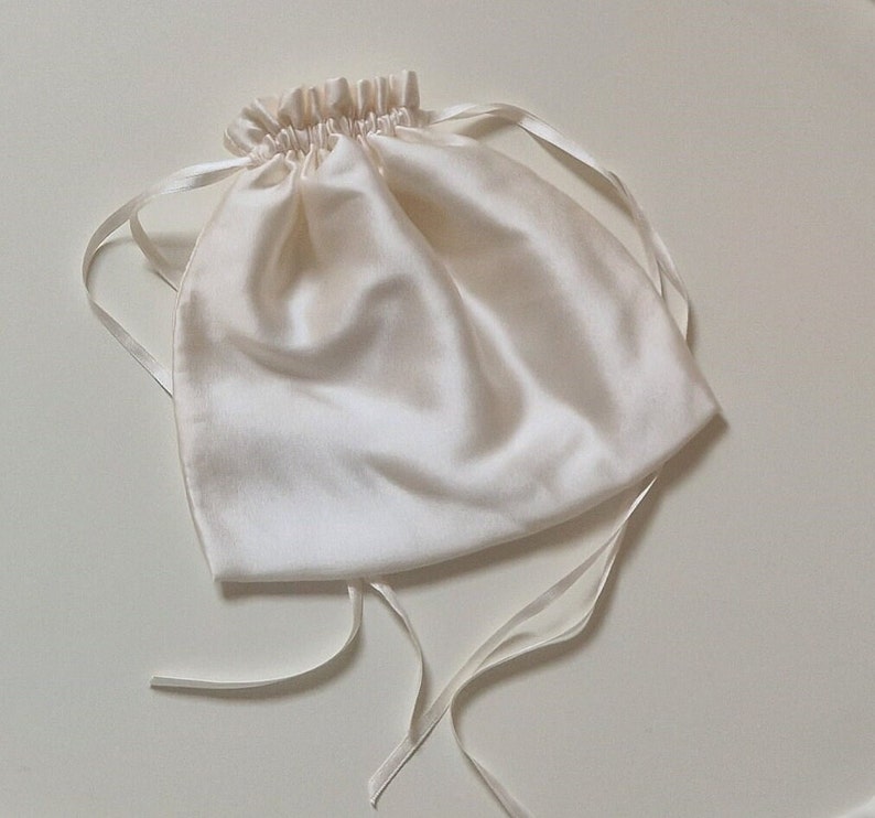 Image of drawstring silk bag which comes with the wedding garter. It is made from soft white silk, with long narrow silk ribbons and is shown closed and gathered.