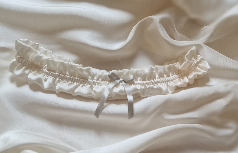 Soft white, pure silk wedding garter adorned with a graceful silver silk bow at its centre.