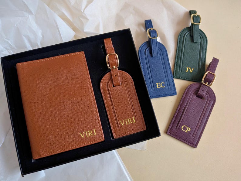 A brown passport cover and luggage tag set in a black gift box with the name VIRI embossed in gold next to luggage tags showing other colors: navy, green, and burgundy all with gold embossing.