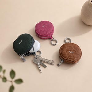 Three zipper coin pouches with keyring attachments in green, pink, brown.