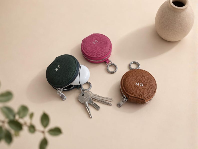 Three zipper coin pouches with keyring attachments in green, pink, brown.