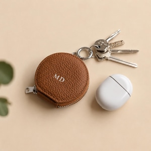 Keychain zip pouch in brown leather with initials MD shown next Apple Airpods.