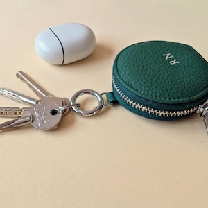 Keyring zip wallet in green leather with initials RN shown next Apple Airpods.