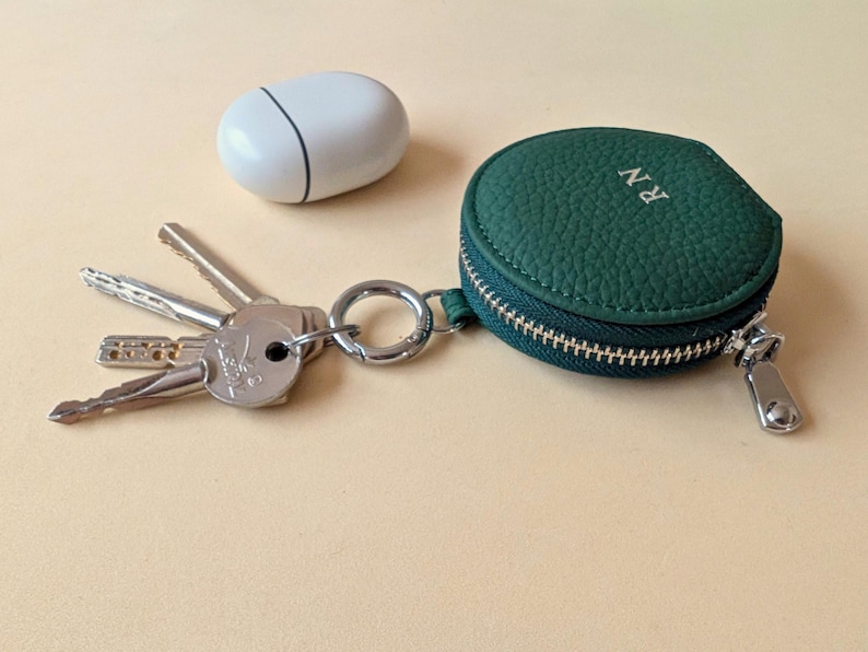 Keyring zip wallet in green leather with initials RN shown next Apple Airpods.