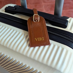 Brown luggage tag on a suitcase with custom initials.