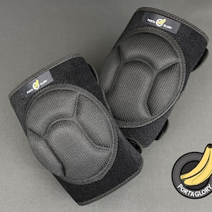 May include: Two black knee pads with a honeycomb-like texture and the text "PORTA GLORY" on the side. The knee pads are on a gray surface.