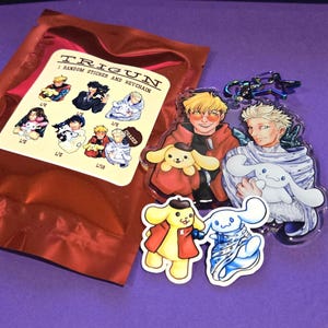May include: A red package with a sticker and keychain set featuring anime characters. The sticker sheet has multiple character designs. Two clear acrylic keychains and two stickers of cartoon characters are also visible.