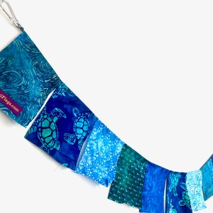 May include: A blue and green fabric banner with a sea turtle pattern. The banner is strung on a white background. The banner has a tag that says "JoyfulFlags.com".