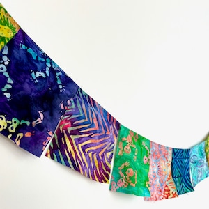 May include: A colorful fabric banner with a variety of patterns and colors, including green, blue, purple, and yellow. The banner is made of squares of fabric sewn together.