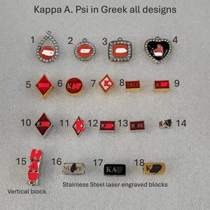 May include: A collection of 18 different designs of Kappa Alpha Psi fraternity pins. The pins are made of metal and feature various colors, including red, gold, black, and white. The pins are numbered 1 through 18.
