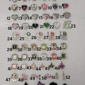 May include: A collection of fifty-seven metal charms featuring various designs, including hearts, squares, and silhouettes, with text such as AKA, LOVE, and Skee Wee. The charms are arranged in rows and numbered one through fifty-seven on a white background.