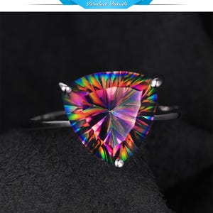 May include: A silver ring featuring a large, triangular-cut gemstone with a vibrant, iridescent rainbow effect. The gem's facets catch the light, displaying a spectrum of colors. The ring is set against a dark background.