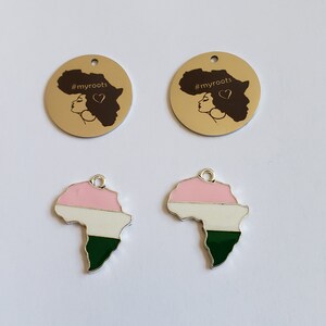 May include: Two gold-colored metal charms with the text "#myroots" and a silhouette of a woman's face with an afro. Two silver-colored metal charms shaped like the continent of Africa with pink, white, and green enamel paint.