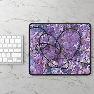 Könnte beinhalten: Lila und schwarzes Mauspad mit einem schwarzen herzförmigen Design. Der Hintergrund ist ein Aquarell in Lila, Rosa und Blau.