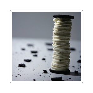 Puede incluir: Una pila alta de galletas Oreo con el relleno de crema hacia afuera. Las galletas están dispuestas en forma de torre sobre una superficie blanca con migas esparcidas.