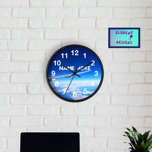 May include: A black and white clock with a blue background featuring a plane flying over clouds. The clock face has white numbers and the text "NAME HERE" in the center.