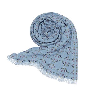 May include: A light blue scarf with a repeating pattern of small animal silhouettes in various colors. The scarf is rolled up and has a fringed edge. The scarf is made of a soft material.