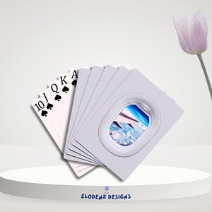 May include: A deck of playing cards with a travel theme. The cards feature the 10, Jack, Queen, King, and Ace of Spades. Some cards have a window design with a view of an airplane wing and the sky. The text "ELODENZ DESIGNS" is at the bottom.