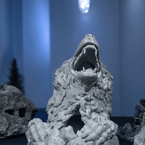 Può includere: Scultura grigia e dettagliata di una testa d'orso con la bocca aperta, che mostra i denti. La testa dell'orso è posta su una base rocciosa. Sfondo blu, con una lampada sopra.