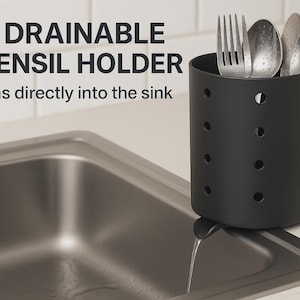 Könnte beinhalten: Ein mattschwarzer, zylindrischer Utensilienhalter mit kreisförmigen Perforationen und einem kleinen Ausguss. Der Text 3D DRAINABLE UTENSIL HOLDER Drains directly into the sink ist sichtbar. Silberne Gabeln und Löffel befinden sich darin.