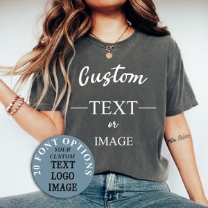 May include: A gray t-shirt with the text "Custom -TEXT- or IMAGE" printed on the front. A circle with the text "20 FONT OPTIONS YOUR CUSTOM TEXT LOGO IMAGE" is visible on the left side of the image.