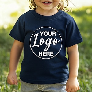 May include: A navy blue toddler's t-shirt featuring a white circular logo with the text "YOUR Logo HERE". The short-sleeved top is made of a soft material, suitable for children.