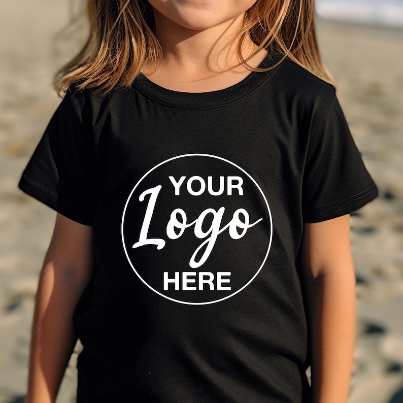 May include: Black crew neck t-shirt with a white circular logo that says "YOUR Logo HERE". The shirt is made of a soft material and is suitable for children. The shirt is a solid black colour.