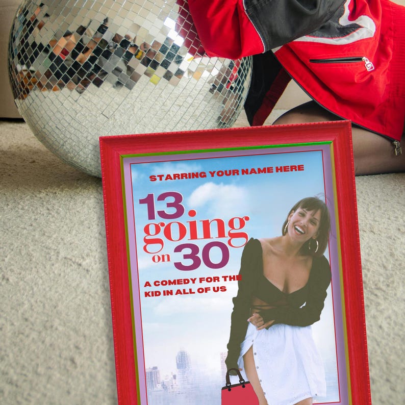 May include: A framed movie poster with a red frame, featuring the text "13 Going on 30". The poster has a blue sky background and a woman smiling. A disco ball is in the background.