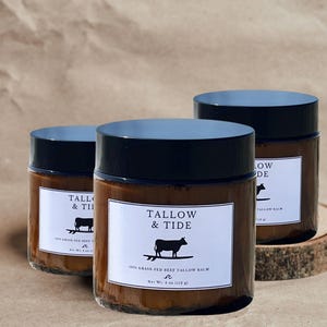 May include: Three glass jars of Tallow & Tide 100% Grass-Fed Beef Tallow Balm with black lids. Each jar has a white label with the brand name, a cow illustration, and the net weight of 4 oz (113 g).