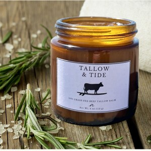 May include: A brown glass jar with a gold lid and a white label that reads "TALLOW & TIDE." The label features a black silhouette of a cow on a surfboard. The jar contains a balm and is surrounded by rosemary and salt. Net Wt. 4 oz (118 g).