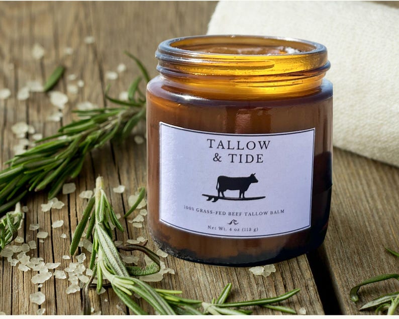 May include: A brown glass jar with a gold lid and a white label that reads "TALLOW & TIDE." The label features a black silhouette of a cow on a surfboard. The jar contains a balm and is surrounded by rosemary and salt. Net Wt. 4 oz (118 g).