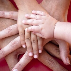 Op de afbeelding: Een stapel van meerdere handen van verschillende groottes, vari&euml;rend van een grote volwassen hand tot een kleine babyhand, allemaal in een centrale groep op elkaar gestapeld. De huidtinten zijn licht tot medium en de vingers zijn in een waaier gespreid.