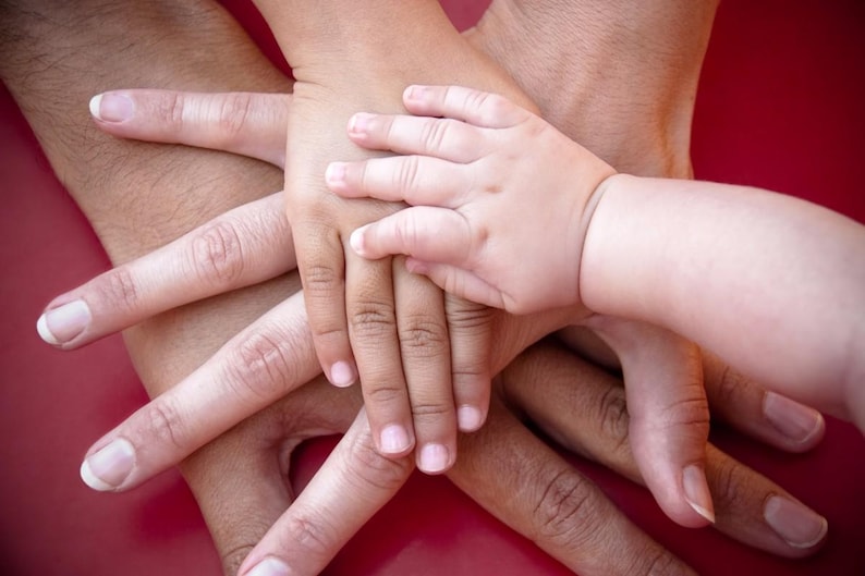 Op de afbeelding: Een stapel van meerdere handen van verschillende groottes, vari&euml;rend van een grote volwassen hand tot een kleine babyhand, allemaal in een centrale groep op elkaar gestapeld. De huidtinten zijn licht tot medium en de vingers zijn in een waaier gespreid.