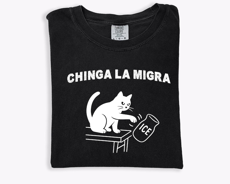 May include: Black t-shirt with white graphic of a cat pushing over an ice jar. The text "CHINGA LA MIGRA" is above the cat illustration. The shirt is folded and has a Comfort Colors tag.