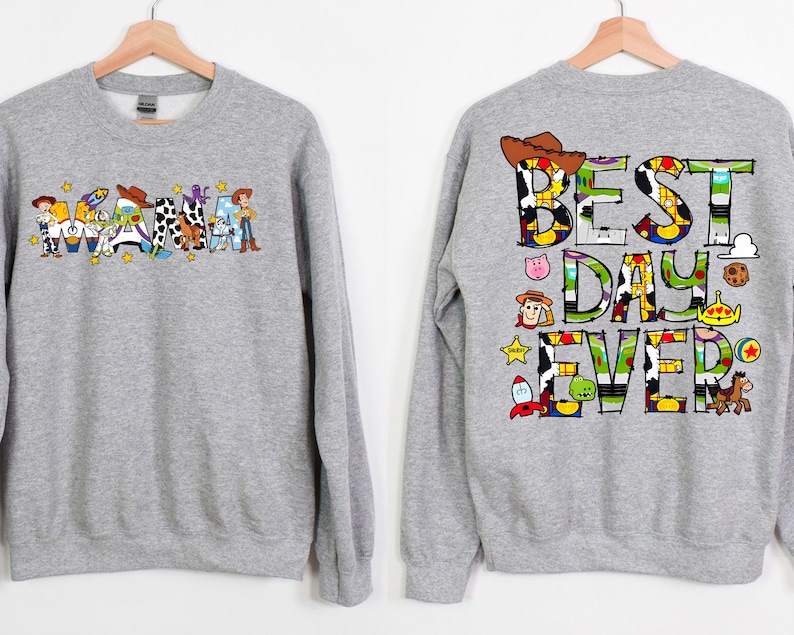 Puede incluir: Sudadera gris con tem&aacute;tica de Toy Story. La parte delantera presenta la palabra "Mama" deletreada con personajes de Toy Story. La parte trasera presenta el texto "Best Day Ever" deletreado con personajes de Toy Story.