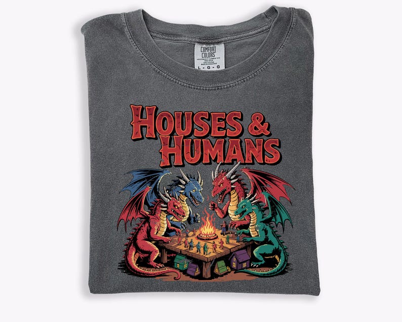 May include: Dark gray t-shirt with the text "HOUSES & HUMANS" in red. The graphic features four dragons of different colors gathered around a table with a bonfire. The shirt is folded on a white surface.