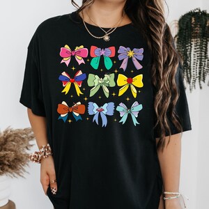 May include: Black t-shirt with a colorful graphic of bows. The bows are in various colors and patterns, including pink, blue, green, yellow, and purple.